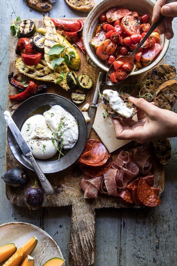 overhead photo of Marinated Tomato and Grilled Veggie Cheese Board with hands in photo