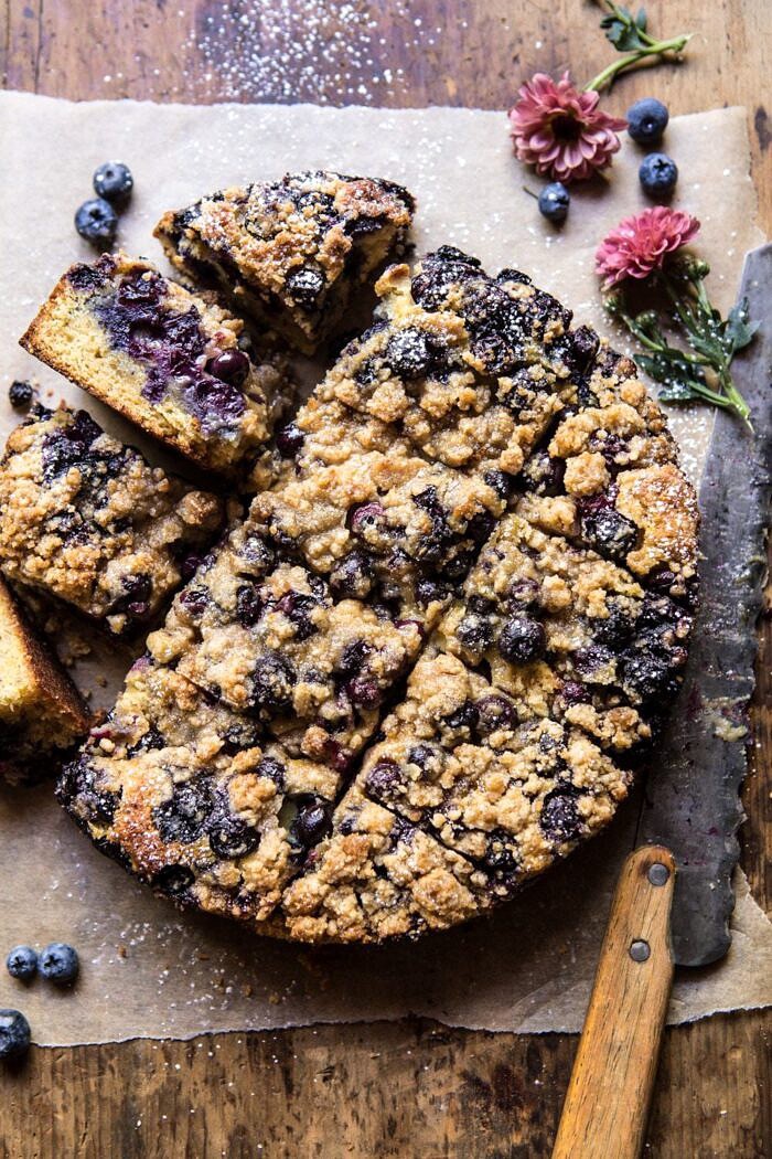 Bursting Blueberry Cardamom Buckle | halfbakedharvest.com #blueberry #cake #summerrecipes #easyrecipes #dessert overhead photo of Bursting Blueberry Cardamom Buckle with knife and flowers in photo