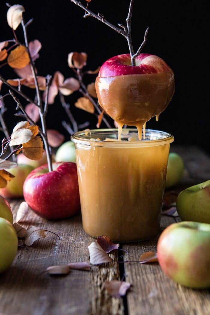 Sweet and Salty Chocolate Drizzled Cider Caramel Apples | halfbakedharvest.com #fallrecipes #apples #caramel #hallaween #thanksgiving apples being dipped in caramel