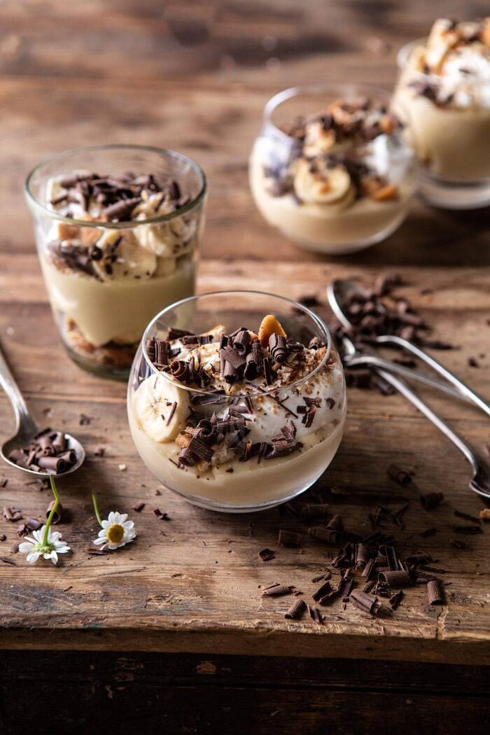 side angled photo of Coconut Banana Cream Pie Parfaits with spoons on table and 4 parfaits in photo