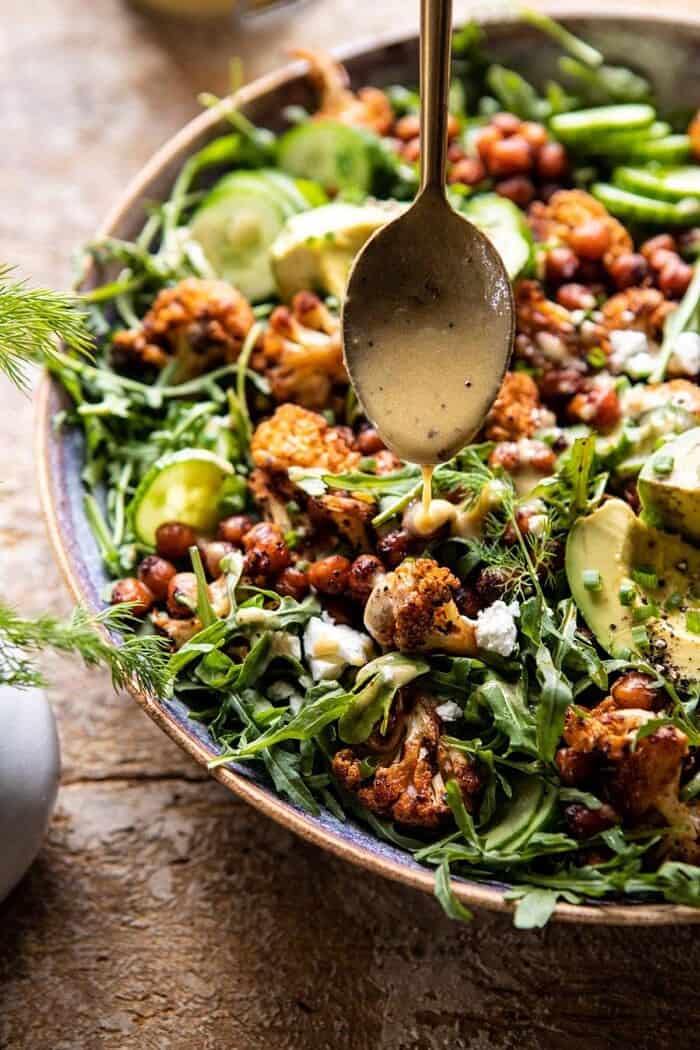 Roasted Cauliflower Salad with Creamy Honey Mustard Vinaigrette | halfbakedharvest.com #healthyrecipes #salad #cauliflower front on action shot of Roasted Cauliflower Salad with Creamy Honey Mustard Vinaigrette being poured onto salad