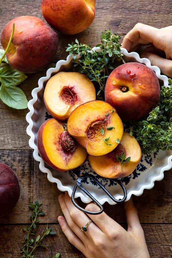 Prosciutto Goat Cheese Stuffed Peaches with Thyme Honey | halfbakedharvest.com #peaches #appetizer #goatcheese overhead photo of peaches in bowl with hands on bowl