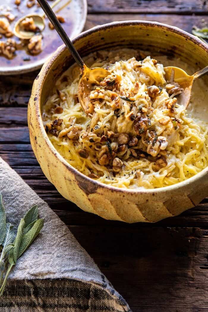 Creamed Spaghetti Squash with Browned Butter Walnuts | halfbakedharvest.com #spaghettisquash #healthy #thanksgiving #sage side angled photo of Creamed Spaghetti Squash with Browned Butter Walnuts with hands pulling up the spaghetti squash