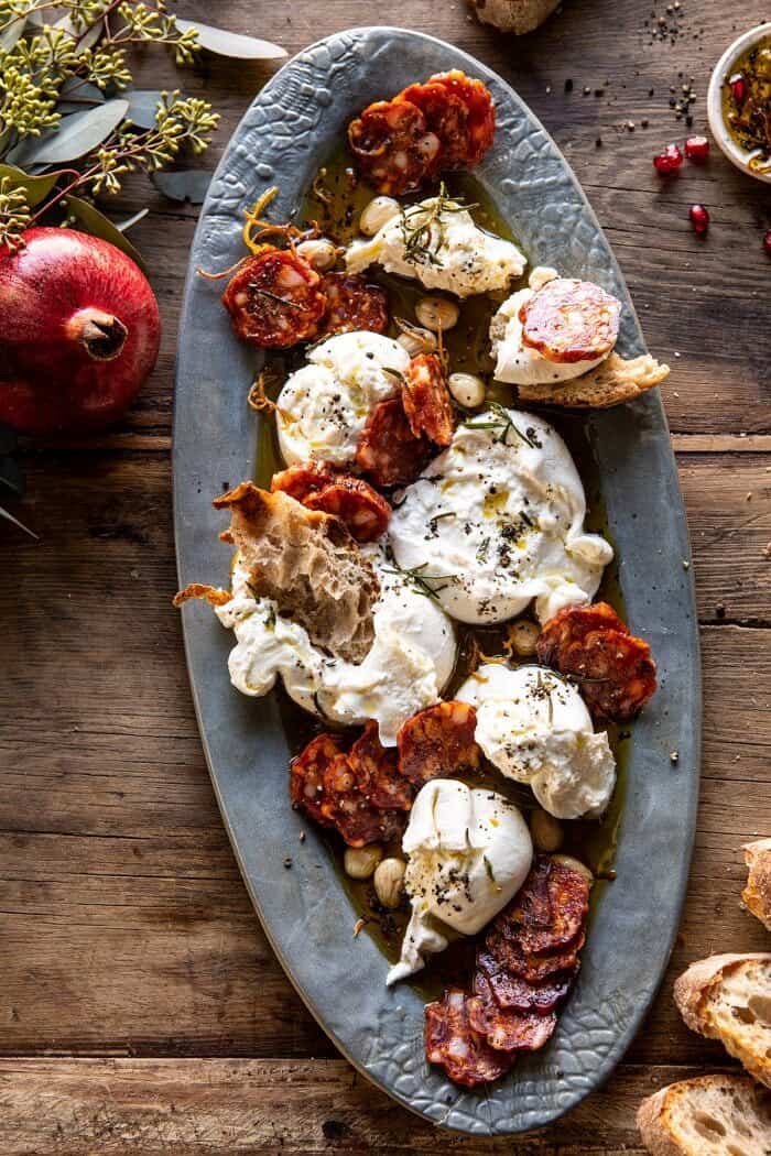 overhead photo of Burrata with Lemon Pepper Salami Bites on serving plate with pomegranate on table
