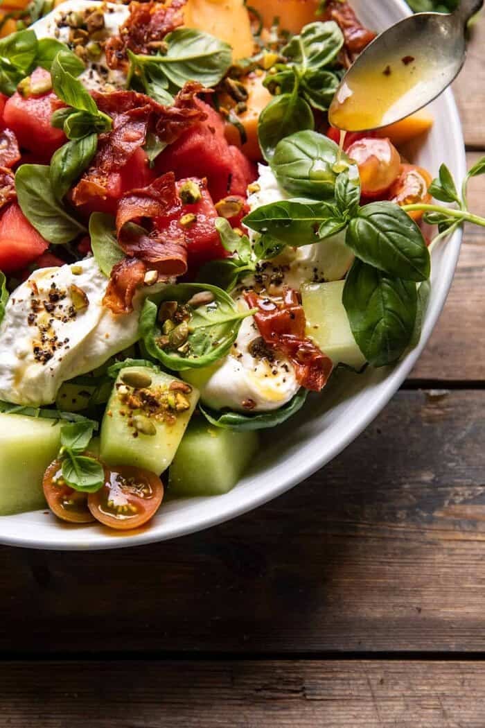 side angle action photo of Melon Basil Burrata Salad with Crispy Prosciutto with dressing being added