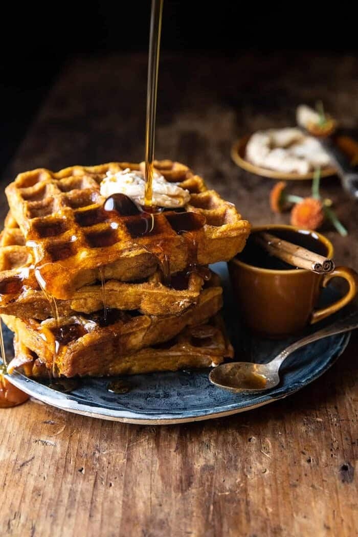 Cider Pumpkin Waffles with Salted Maple Butter | halfbakedharvest.com side angled action photo of Cider Pumpkin Waffles with Salted Maple Butter (the maple is being poured on the waffles)