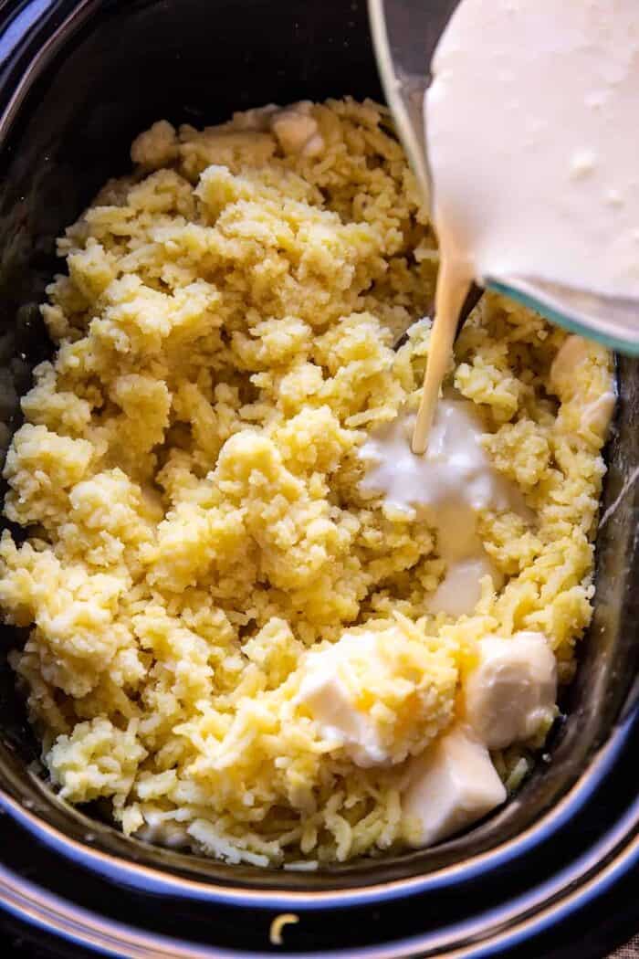 Slow Cooker Cheesy Garlic Herb Mashed Potatoes | halfbakedharvest.com prep photo of cream being added to potatoes