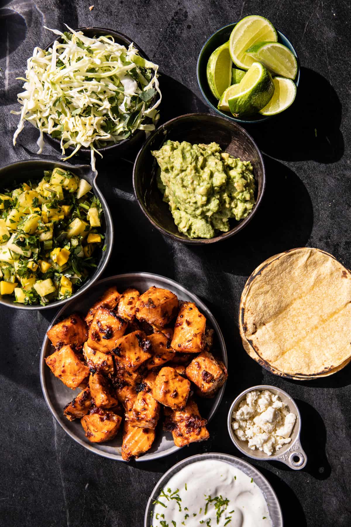 overhead photo of ingredients, roasted salmon, pineapple salsa, avocado, cabbage, tortillas, crema, limes, cheese